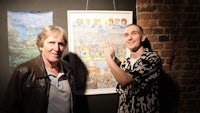 two men standing next to a painting on a wall